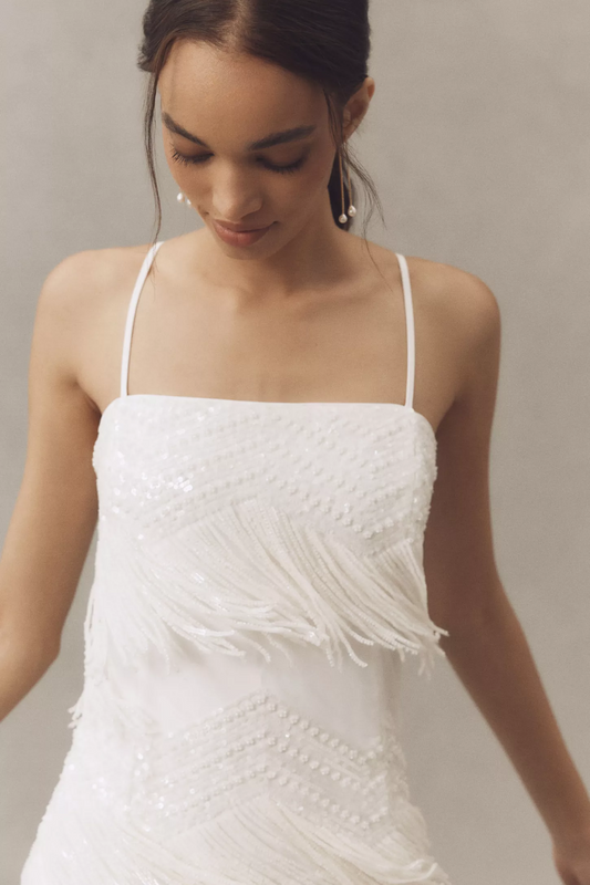 Woman wearing a white dress with fringe details against a neutral background